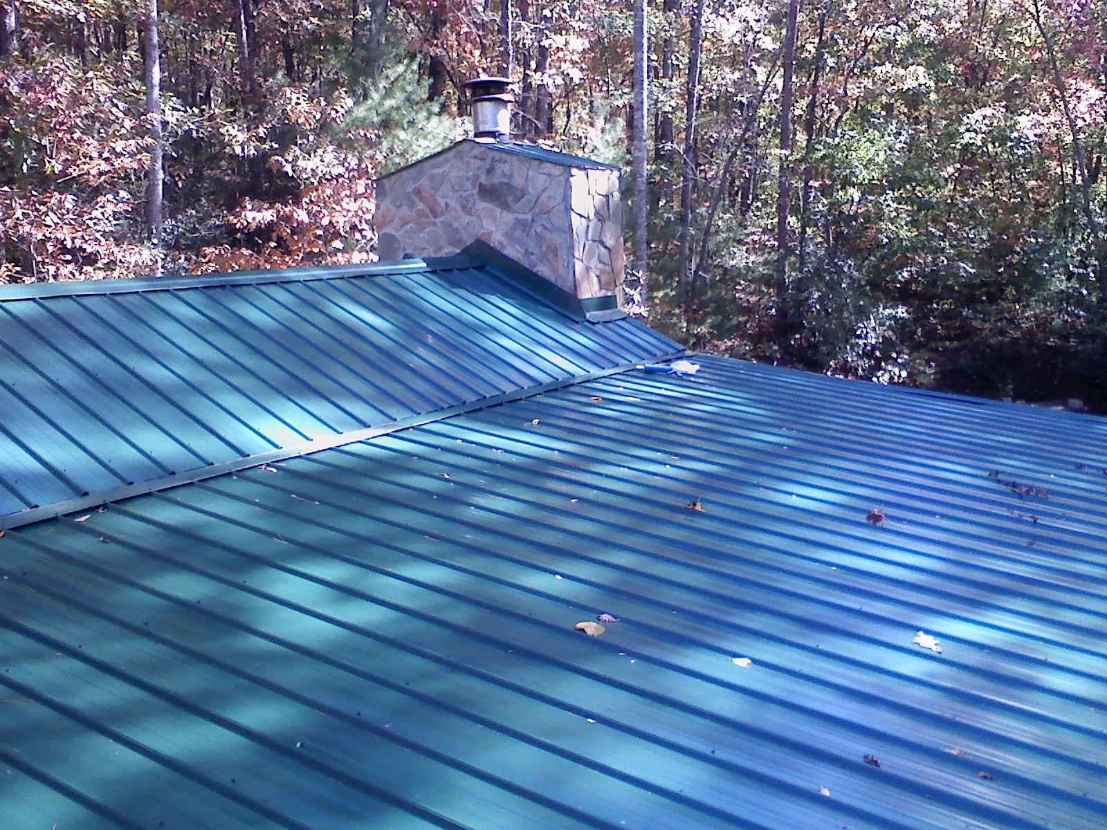 New green metal roof and stone chimney surrounded by autumn woods in Andover